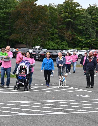 Several people wearing pink shirts walk together on a concrete road.