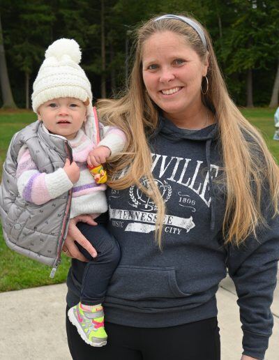 A woman with light skin tone and long, blond hair holds an infant with a light skin tone wearing a warm coat and hat.