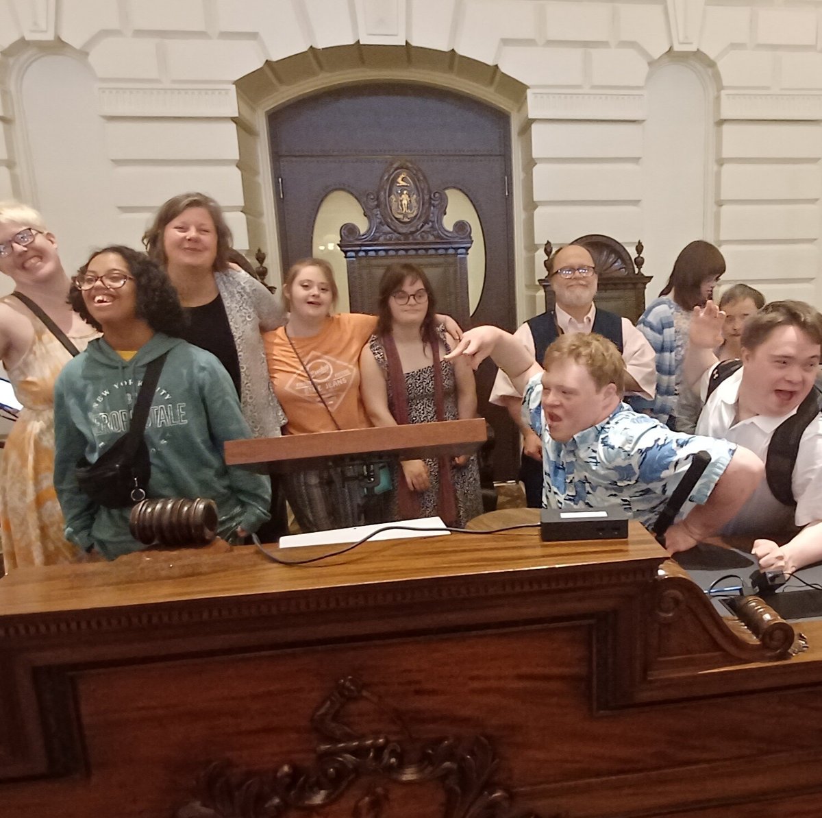 A diverse group of people stand in front of a podium at the Massachusetts State House.
