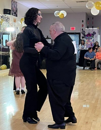 Michael Cooley, an older with a disability and a light skin tone with short gray hair, dances with a woman with a light skin tone and shoulder-length black hair.
