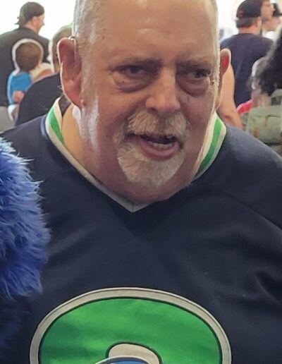 Portrait of Michael Cooley, an older man with a disability, light skin tone, and short gray hair wearing a sports jersey.