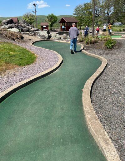 A man with a light skin tone walks toward the end of a mini golf hole.