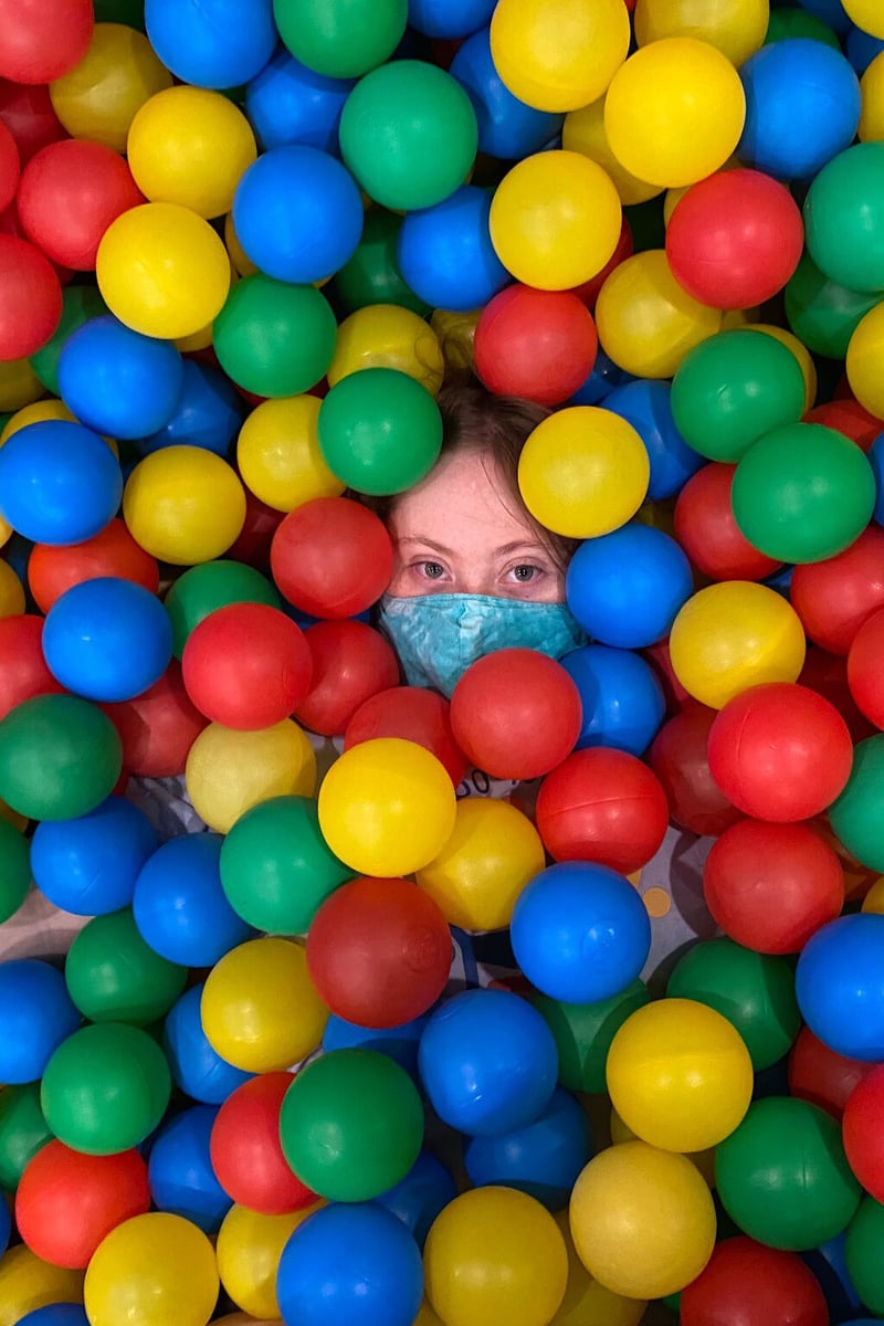 A woman with Down Syndrome and a light skin tone looks directly at the camera while submerged in the ball pit at the Northampton Inclusive Community Center.