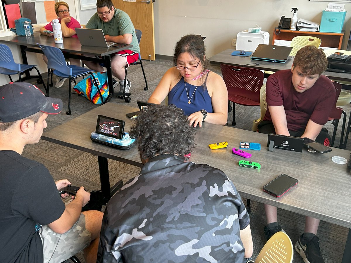 Four diverse people sit at a table playing various Nintendo Switch video games.